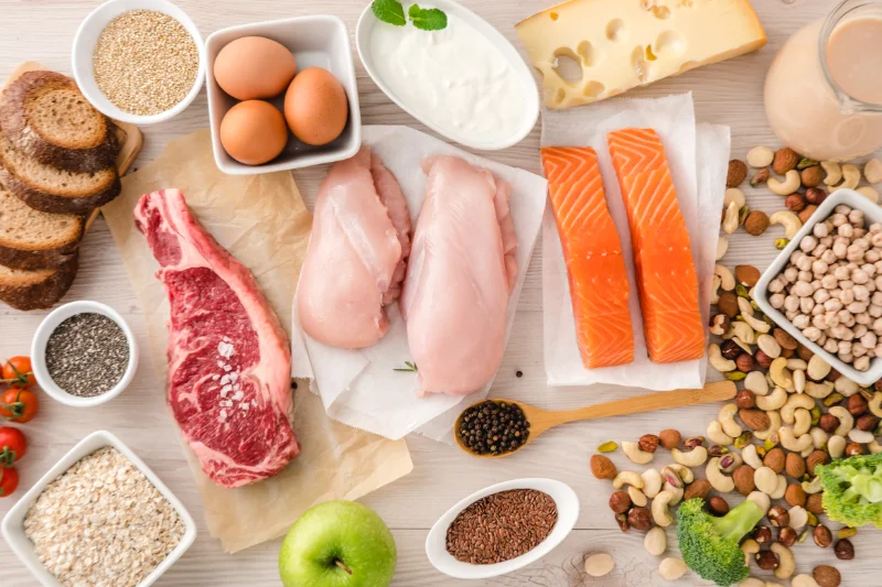 Selection of animal and plant protein sources including chicken, salmon, beef, eggs, dairy, nuts, grains, and vegetables.