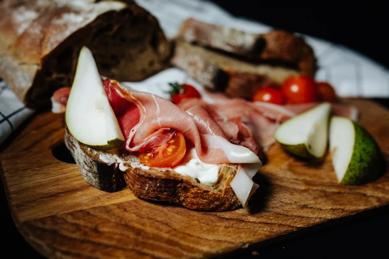 Homemade sandwich topped with ham, pear slices, and cherry tomatoes on rustic bread