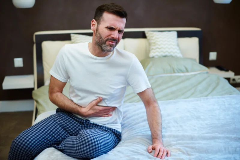 Man sitting on bed holding his stomach in pain from eating heavy late-night food