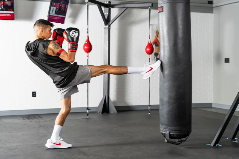 Man Kicking Heavy Bag at 9Round HIIT Workout Athlete practicing a high kick on a heavy bag during a 9Round HIIT workout.