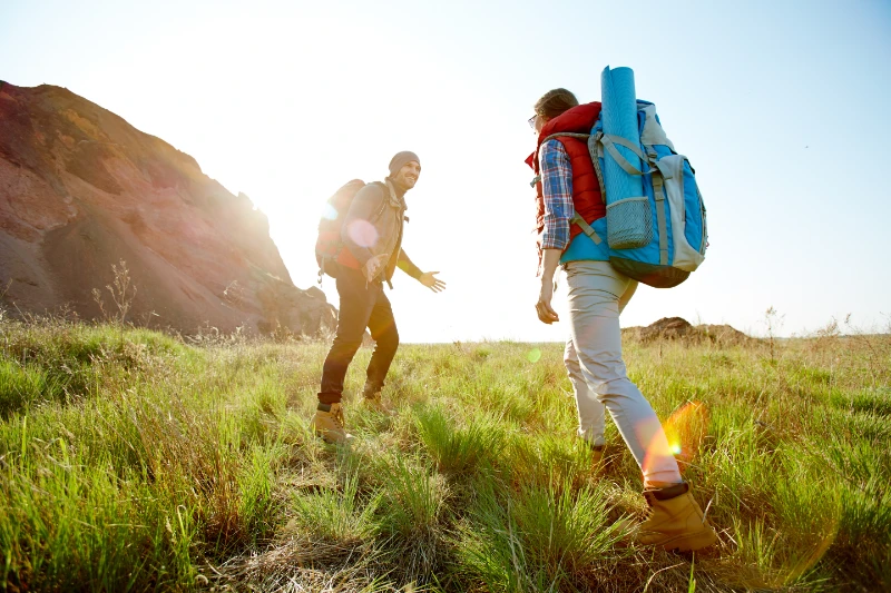 Two hikers with backpacks walking across grassy terrain during an outdoor endurance activity