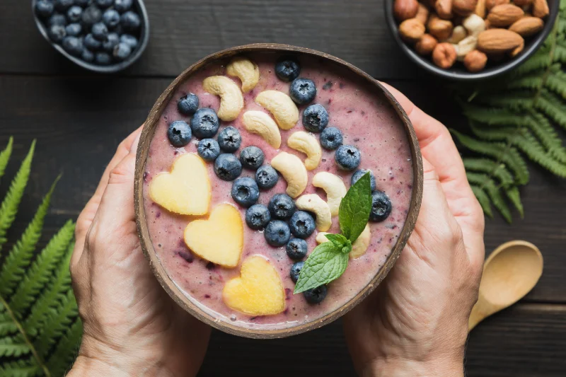 Smoothie bowl with blueberries, cashews, and peach hearts decorated with mint