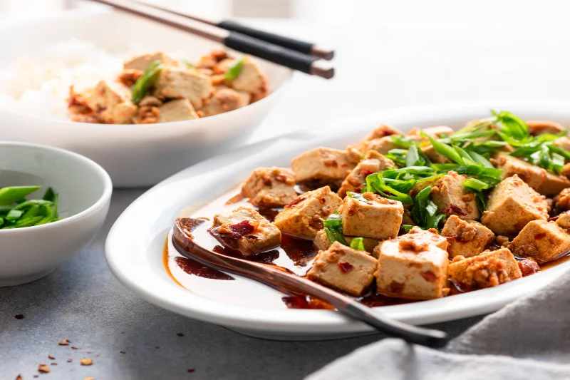 Plate of spicy tofu cubes topped with green onions, a rich source of soy protein.