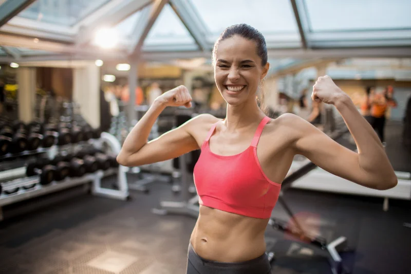 Smiling woman flexing her arms at the gym while preparing for wedding fitness goals.