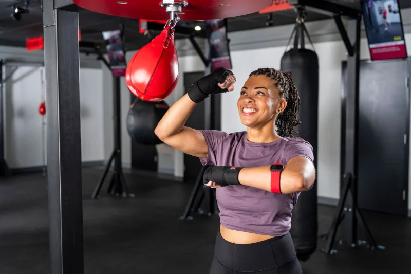 Woman Using Speed Bag in 9Round HIIT Workout Smiling woman working out with a red speed bag at 9Round during a HIIT session.