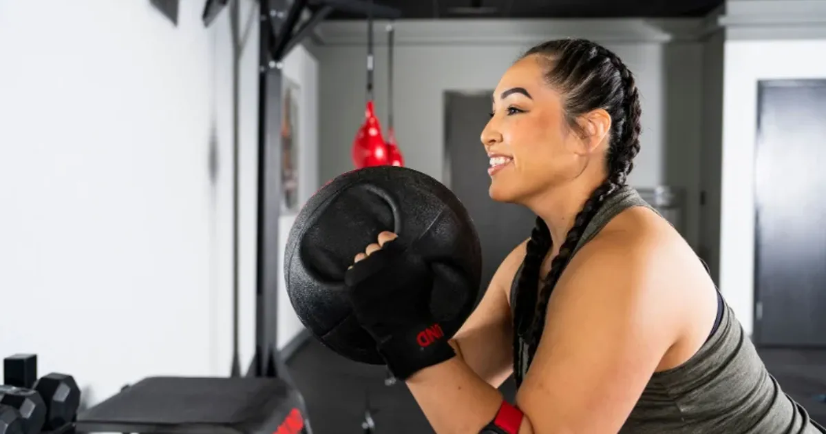 Woman performing a medicine ball exercise at 9Round during a guided HIIT circuit training workout