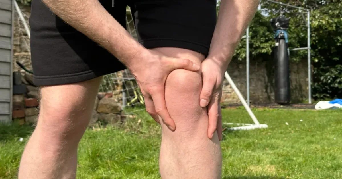 Close-up of a person holding a sore knee outdoors after activity.