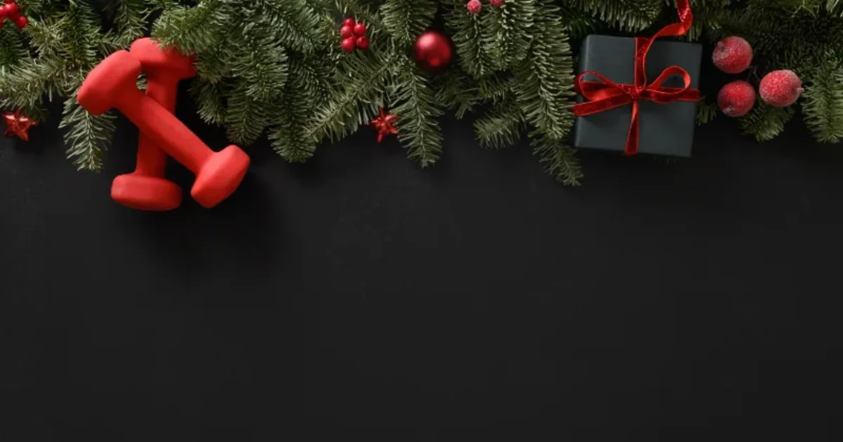 Red dumbbells surrounded by Christmas greenery representing holiday fitness and staying active during December