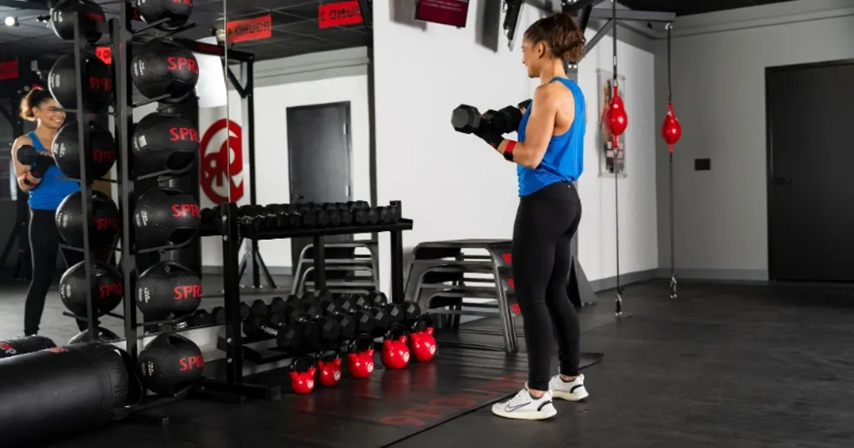 Woman performing strength training with dumbbells inside a 9Round Fitness studio surrounded