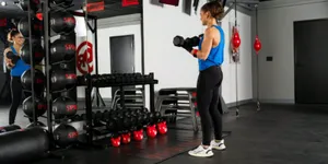 Woman performing strength training with dumbbells inside a 9Round Fitness studio surrounded