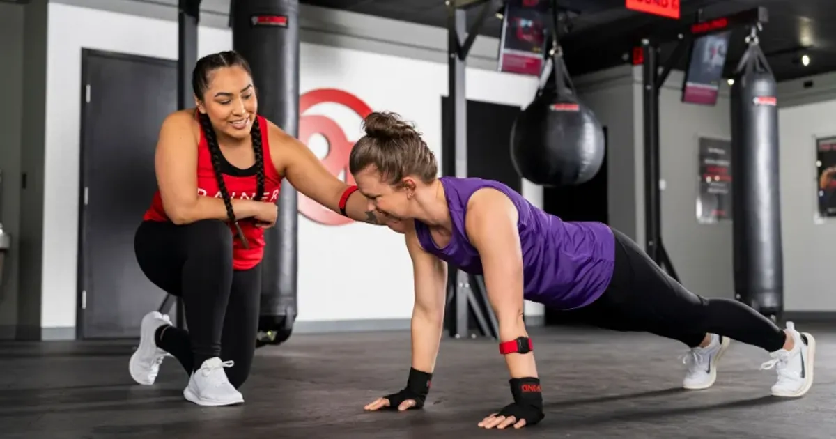 9Round trainer supporting a member during a push-up bodyweight workout
