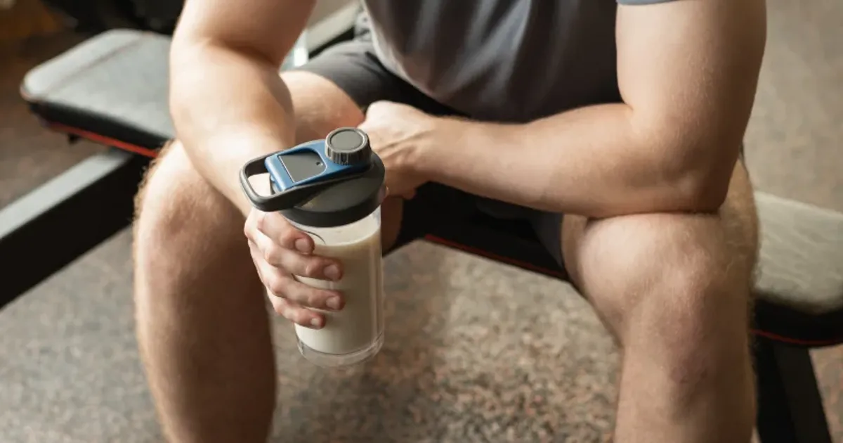 Man in gym holding a protein shake bottle after strength training session.