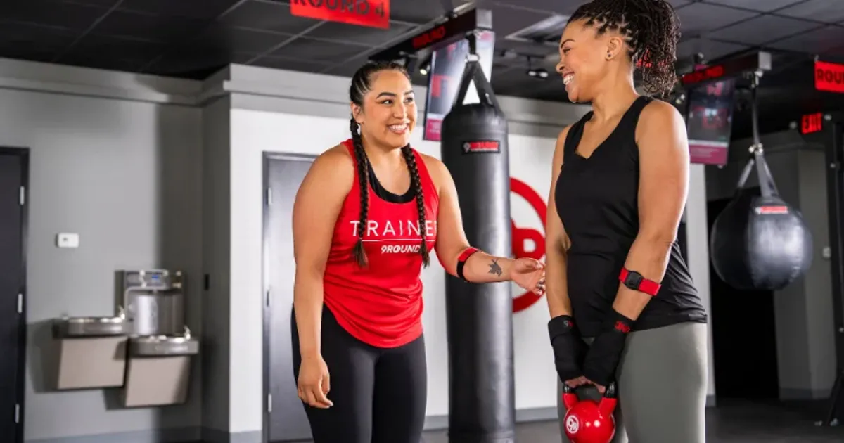 9Round trainer coaching a smiling member using a kettlebell during class.