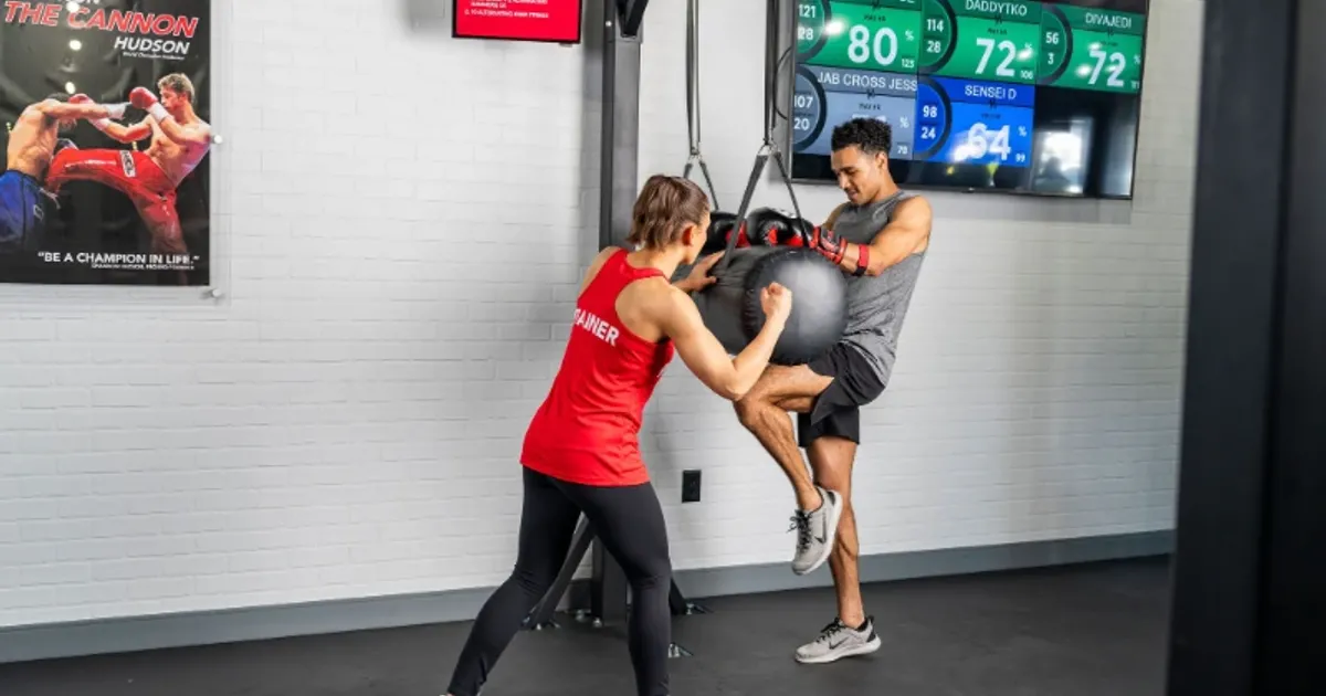 9Round trainer holding a stability ball while a member performs a knee drive during a HIIT session