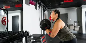 Woman performing a medicine ball squat exercise inside a 9Round Fitness gym