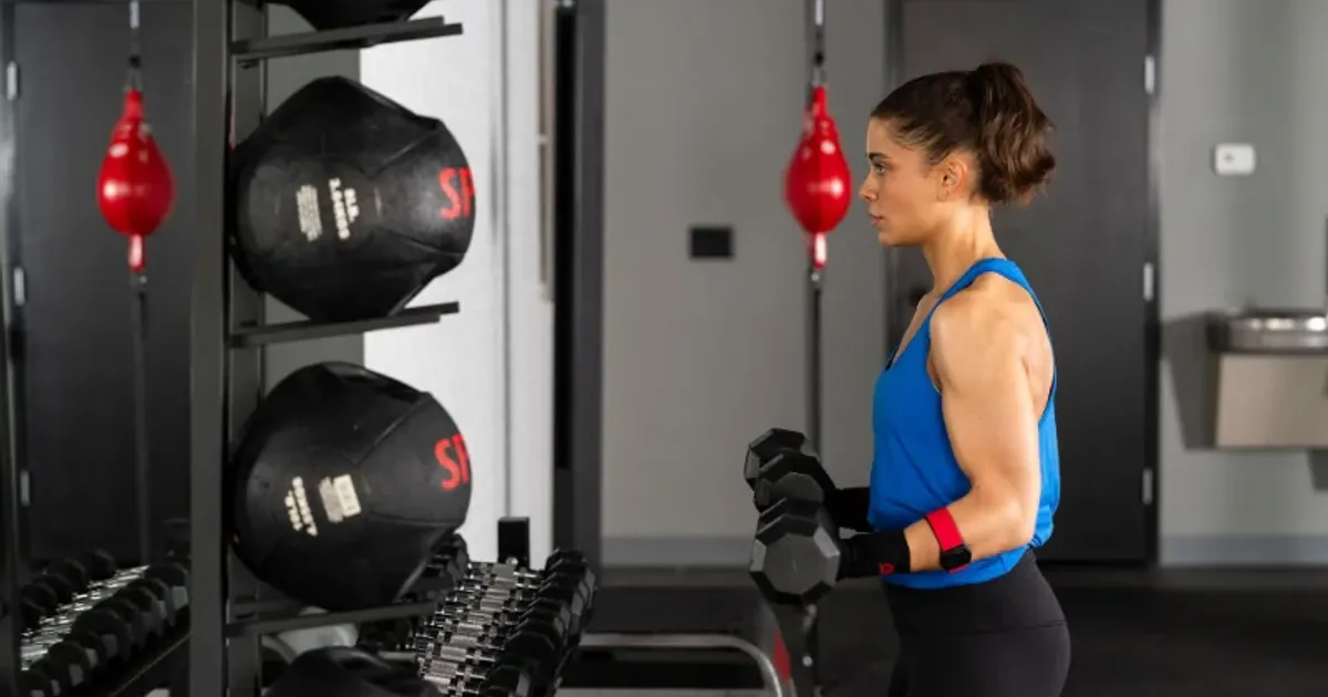 Woman performing a dumbbell strength exercise at 9Round as part of a quick HIIT workout for a busy schedule