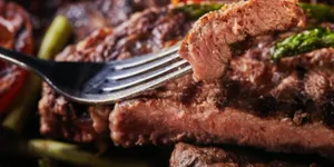 Close-up of grilled beef steak on a fork with roasted vegetables for a carnivore diet meal