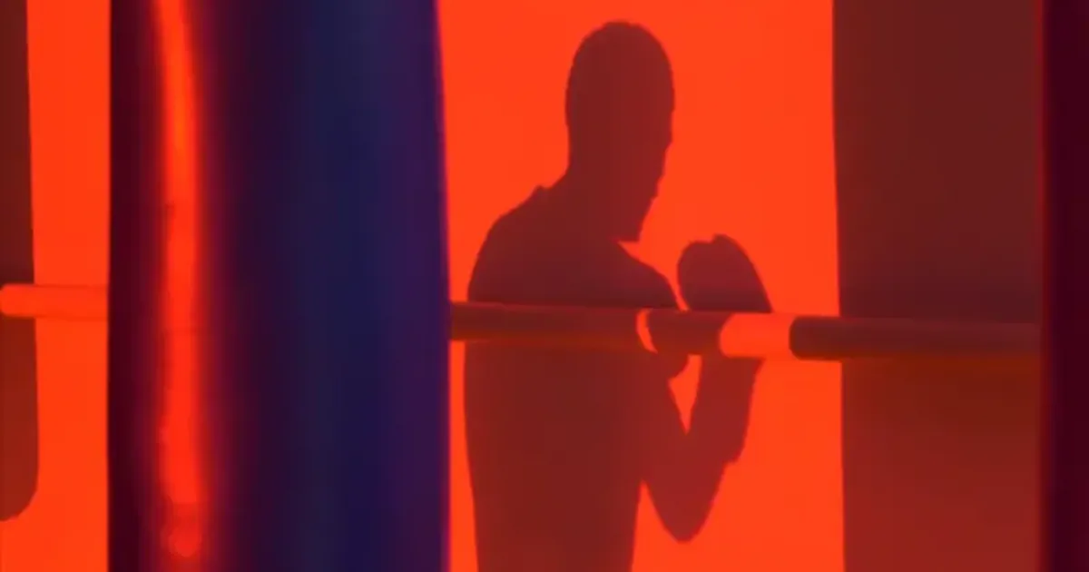 Silhouette of a boxer punching a heavy bag under red light during an intense workout