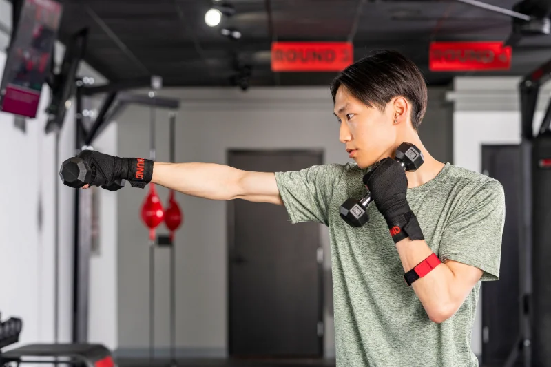 Combine strength and cardio with dumbbell shadowboxing at 9Round Man shadowboxing with dumbbells while wearing 9Round PULSE heart rate monitor in gym