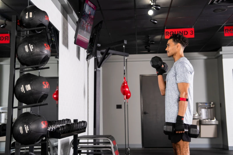 Man performing functional strength exercises with dumbbells during a 9Round Fitness circuit workout inside the gym