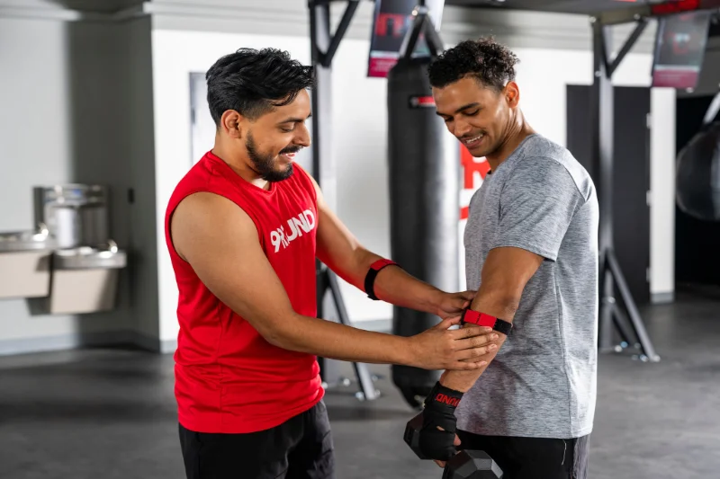 9Round trainer assisting a member with heart rate monitor strap before workout.