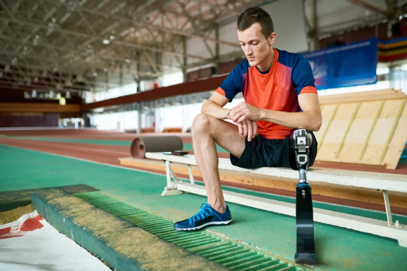 Athlete with a prosthetic leg sitting on a bench at an indoor track after a HIIT workout