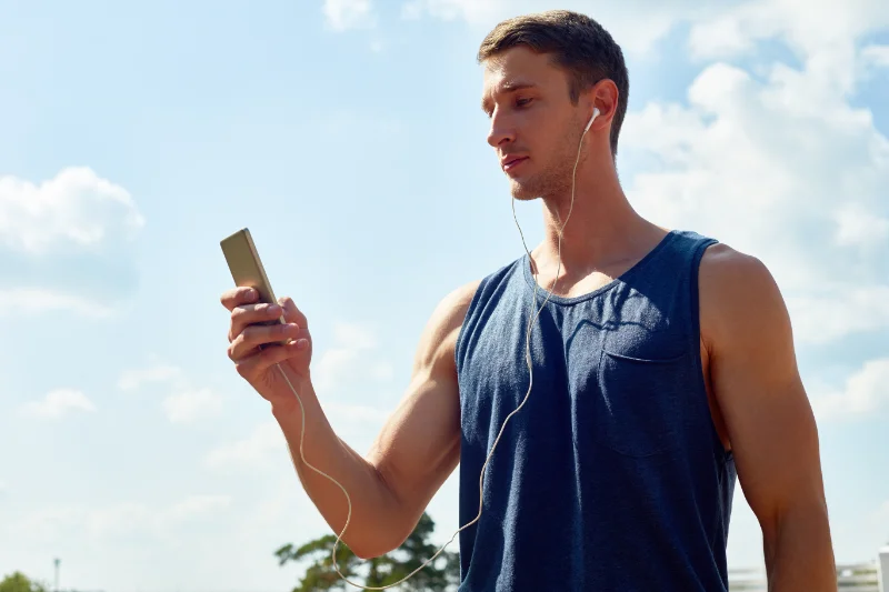 Man in workout gear using phone with earphones for 9RoundNOW virtual training outdoors