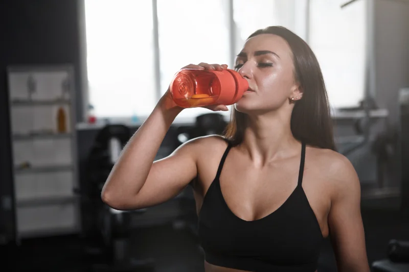 Sportswoman Drinking Water During Workout Fit woman in sportswear drinking water from bottle during workout at gym