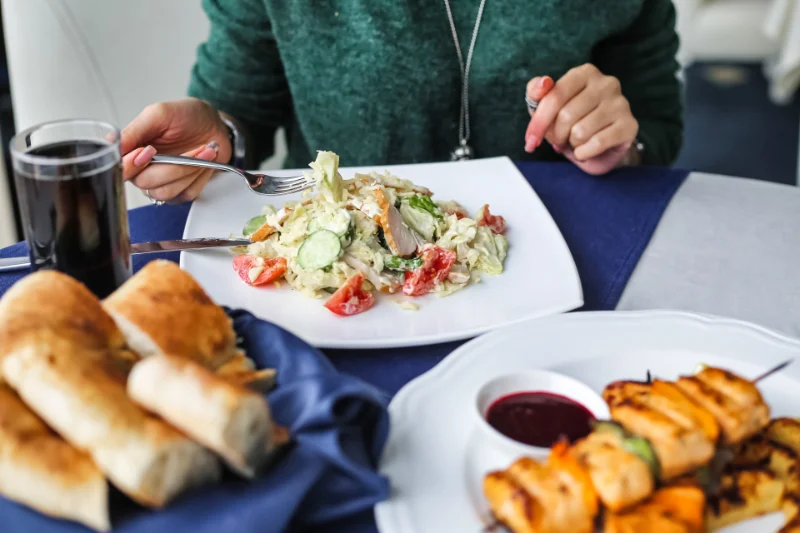 Plate of salad with bread and grilled kebabs served with drink on student's table.